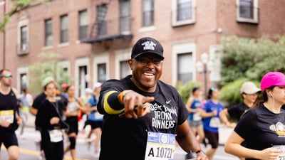 A runner is a Boogie Down Bronx runners t-shirt smiles and points at the camera during the RBC Brooklyn Half
