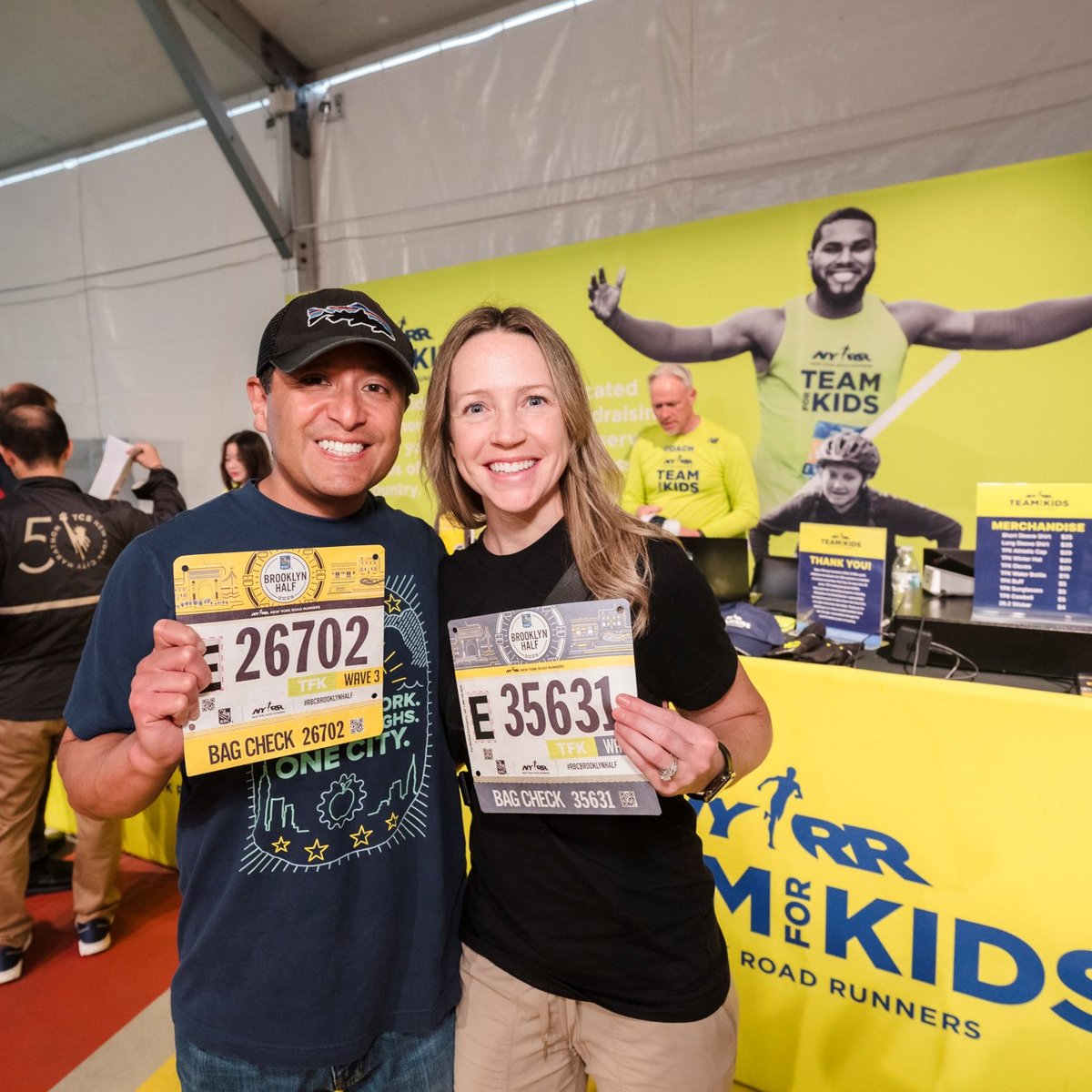 Two runners pose with their bibs in front of the Team for Kids booth at the 2025 RBC Brooklyn Half Pre-Party