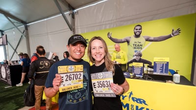 Two runners pose with their bibs in front of the Team for Kids booth at the 2025 RBC Brooklyn Half Pre-Party