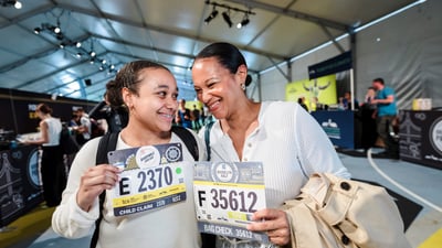 A mom and daughter smile at each other holding their bibs at the 2025 RBC Brooklyn Half Pre-Party