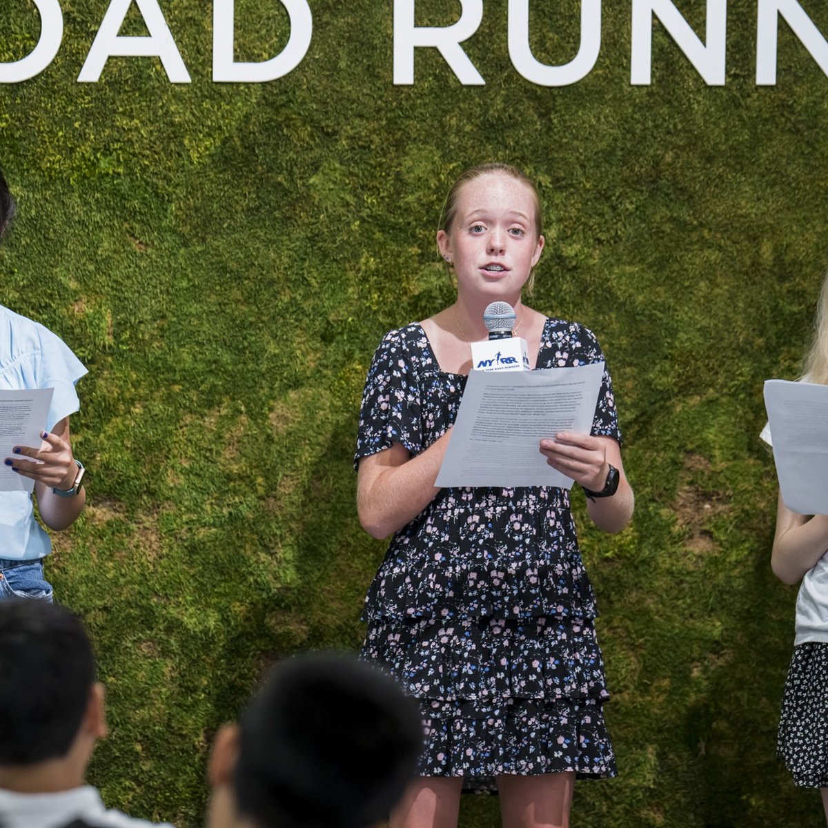 Youth ambassadors with mics and papers speaking at the youth ambassador graduation