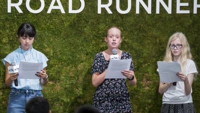 Youth ambassadors with mics and papers speaking at the youth ambassador graduation