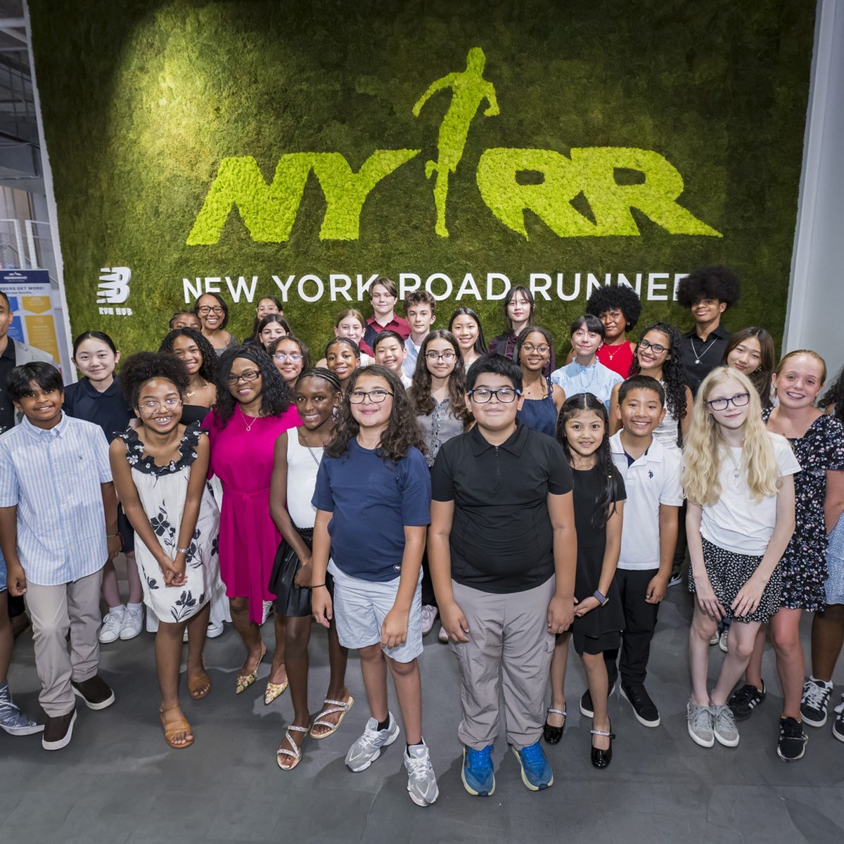 Group shot of youth ambassadors in front of a green grass wall that says NYRR New York Road Runners