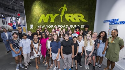 Group shot of youth ambassadors in front of a green grass wall that says NYRR New York Road Runners