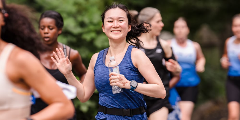 Young woman runner with others in background at summer 2025 NYRR Unlock Group Training session