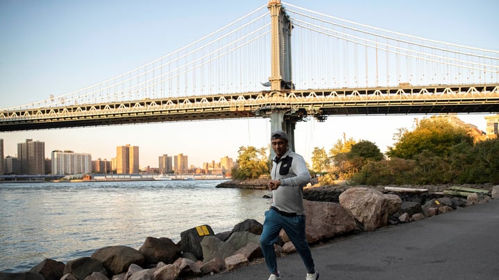 Man looks down at his watch while running on a path next to the water