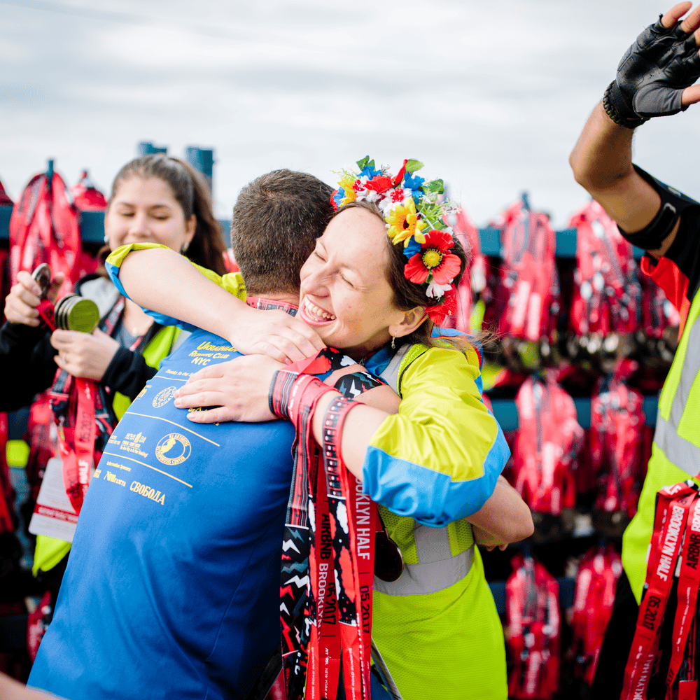 A volunteer with a flower crown hugs a runner at the finish line where medals are being distributed