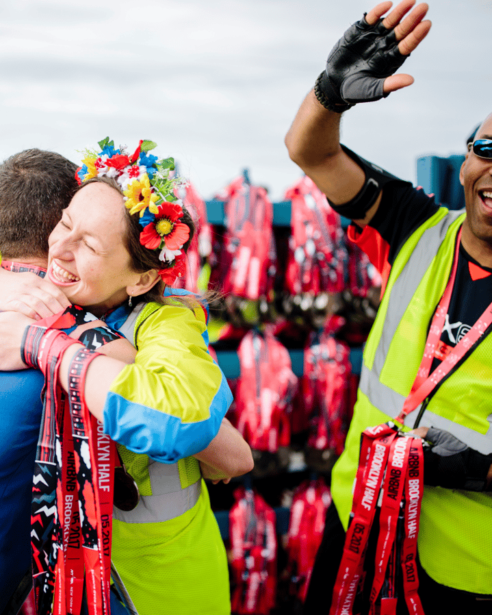 A volunteer with a flower crown hugs a runner at the finish line where medals are being distributed