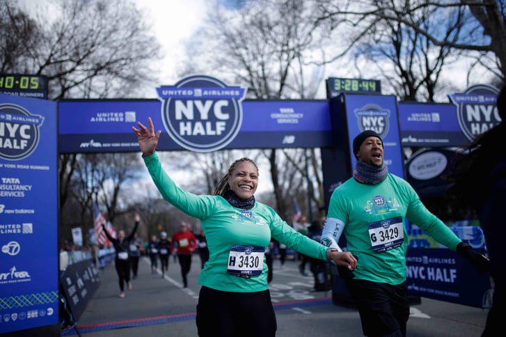 Two runners holding hands at the finish line of the United Airlines NYC Half in Central Park