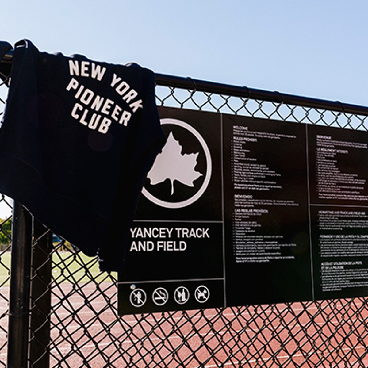 New York Pioneer Club sweatshirt on fence with Yancey Track and Field sign
