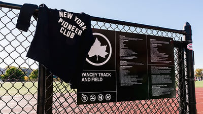 New York Pioneer Club sweatshirt on fence with Yancey Track and Field sign