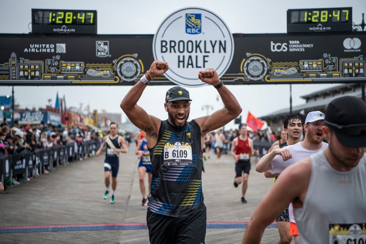 Runner lifts arms in celebration after crossing the Brooklyn Half finish line