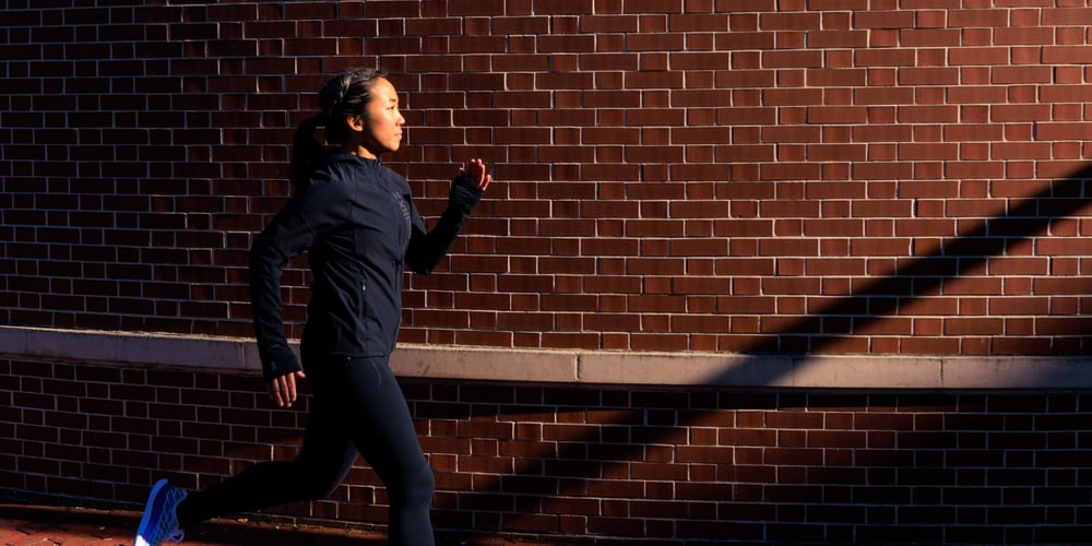 Carolyn Su running with beam of sunlight next to brick wall