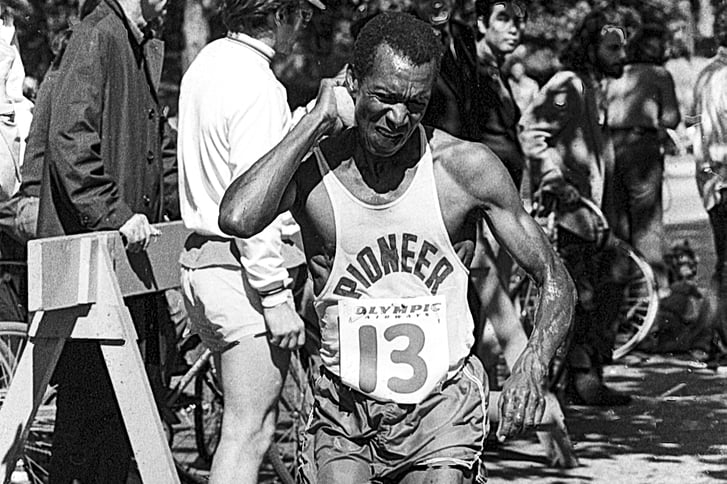 Ted Corbitt running and grimacing Olympic Airways bib