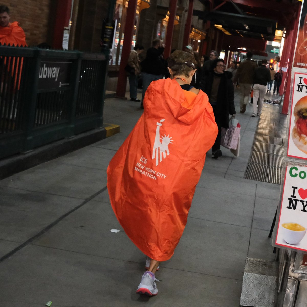 A runner wrapped in their poncho next to a hot dog stand