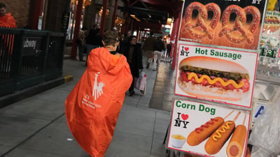 A runner wrapped in their poncho next to a hot dog stand