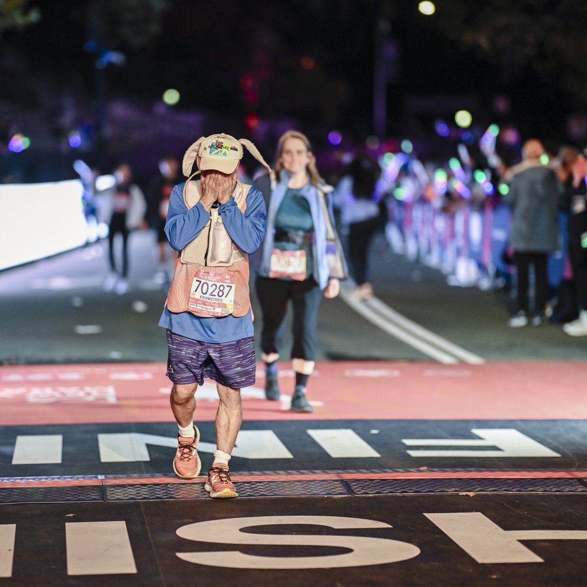 Runner in hat with bunny ears crosses the finish line holding his face