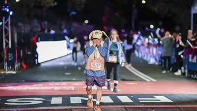 Runner in hat with bunny ears crosses the finish line holding his face
