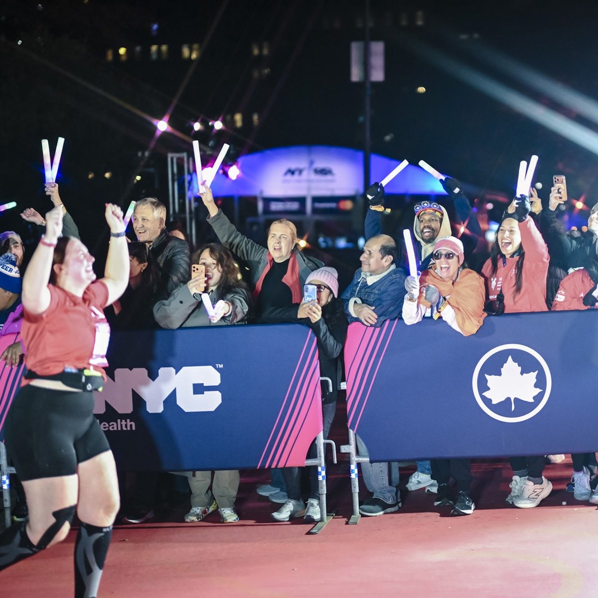 A female final finisher runs through the finish line with her arms up in the air