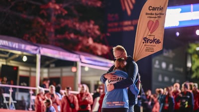 A runner who has a sign that says stroke survivor embraces her partner at the finish line