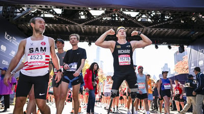 A runner with prosthetic legs flexes his bicep muscle at the finish line of the TCS New York City Marathon