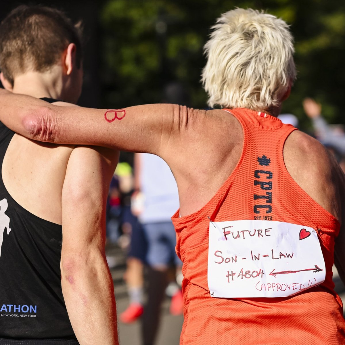 A female runner has her arm around a male runner and she wears a sign on her back that says