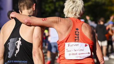 A female runner has her arm around a male runner and she wears a sign on her back that says