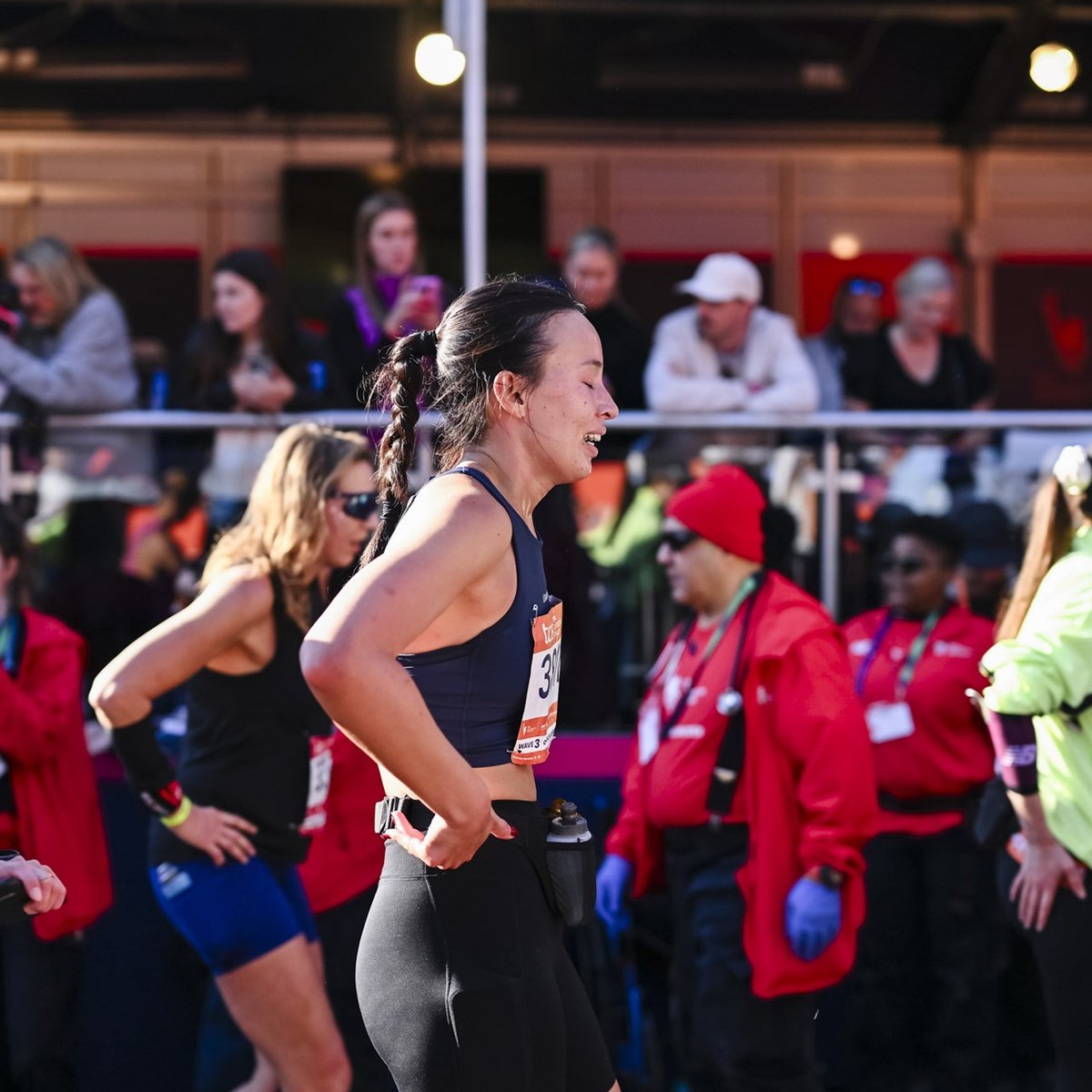 A woman looks relieved as she comes through finish line area at the TCS New York City Marathon with a backdrop of other runners around her