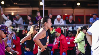 A woman looks relieved as she comes through finish line area at the TCS New York City Marathon with a backdrop of other runners around her