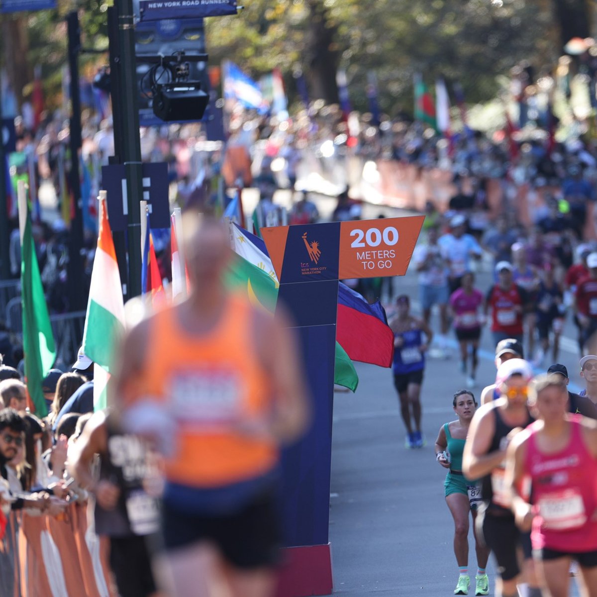 The 200 meters to go sign with some blurry and some in focus runners and spectators in the background
