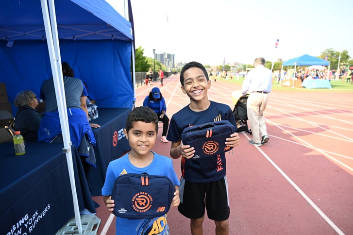 Two children standing on a track holding Rising New York Road Runners lunch boxes