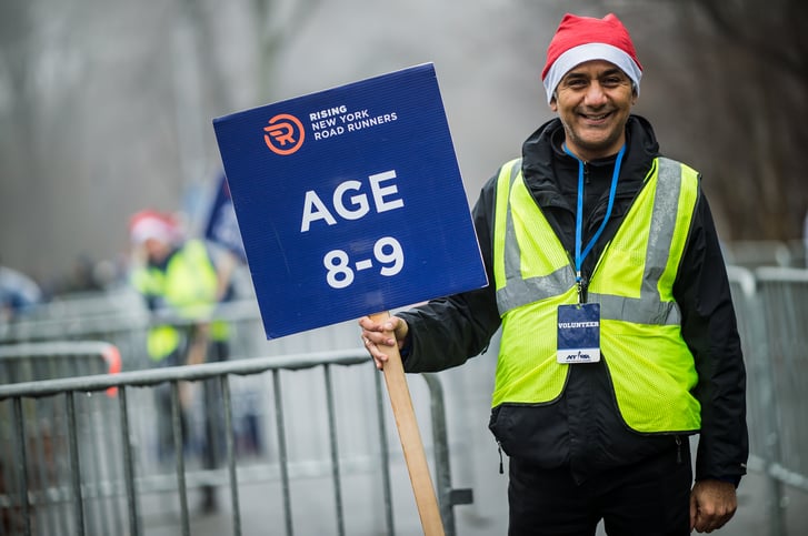 A volunteer holding a sign that says Rising New York Road Runners Age 8-9