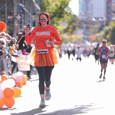 image of anne cosgrove running the tcs nyc marathon in orange running gear representing Fred's Team