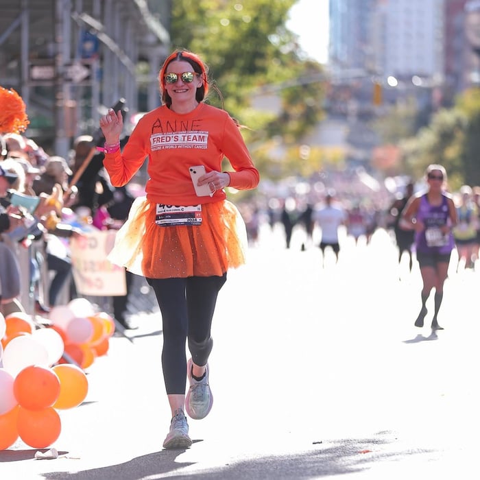 image of anne cosgrove running the tcs nyc marathon in orange running gear representing Fred's Team