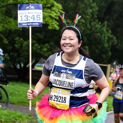 A volunteer pacer runs with a 13:45 pace per mile sign and a rainbow tutu