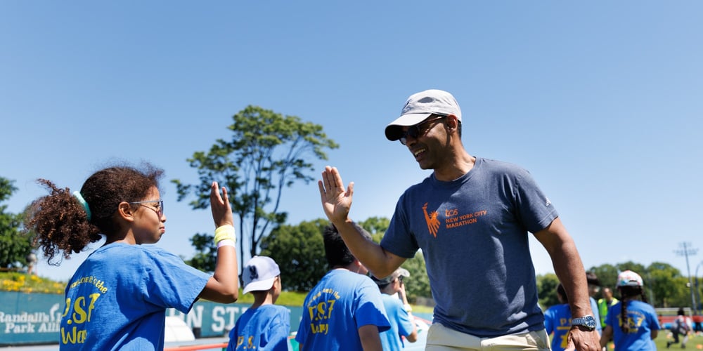 NYRR CEO Rob Simmelkjaer high fiving a child at 2026 Global Running Day at Icahn Stadium in NYC