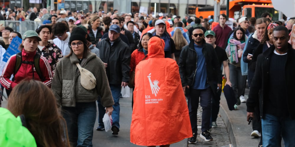 Marathon after 2025 TCS NYC Marathon wearing orange poncho facing away from camera on crowded street.