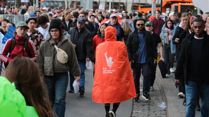 Marathon after 2025 TCS NYC Marathon wearing orange poncho facing away from camera on crowded street.