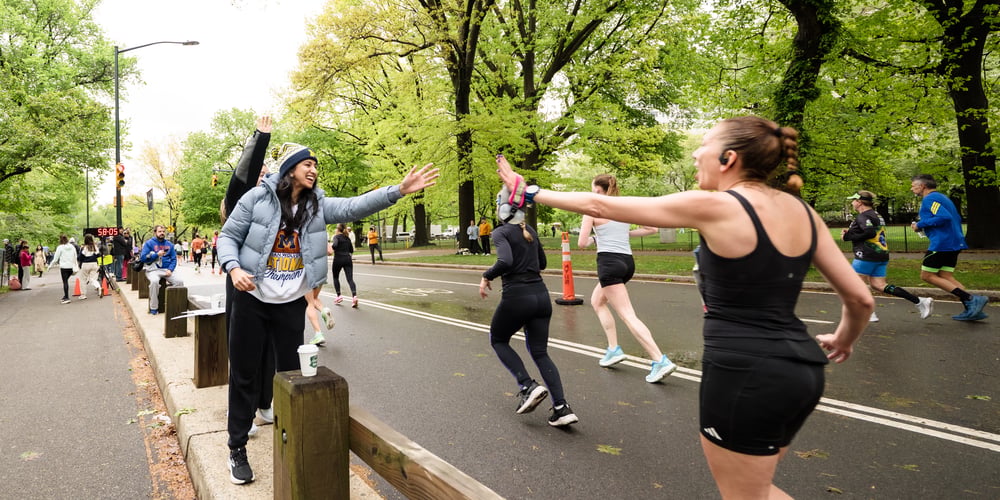 A woman runner high fiving a woman spectator at the 2026 Maybelline Women's Half in Central Park April 2026