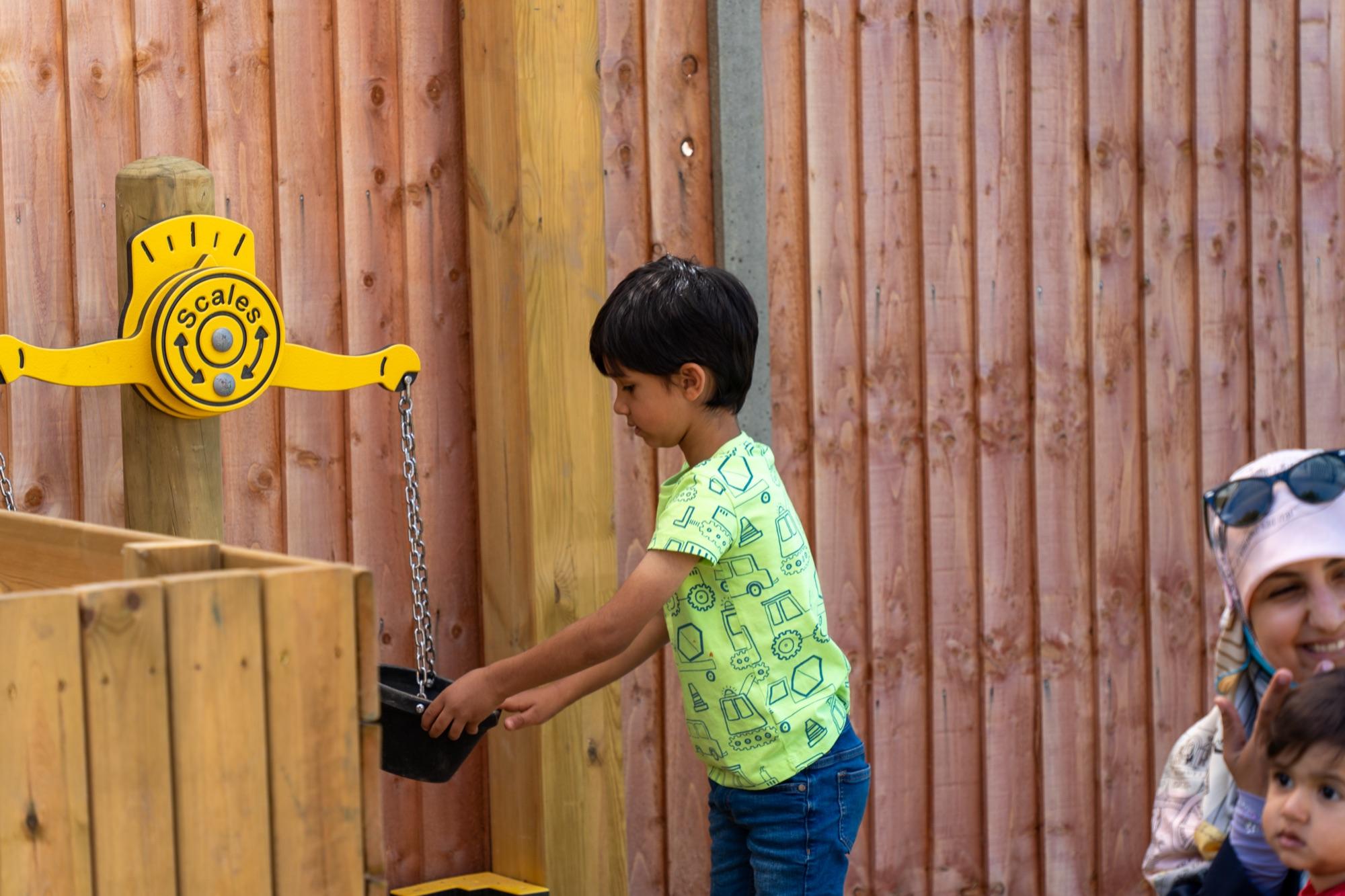 A child weighing and pouring at the outdoor sand station