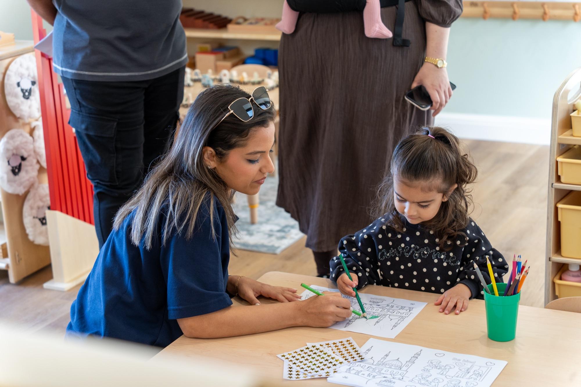 A member of staff drawing alongside a child at a classroom table