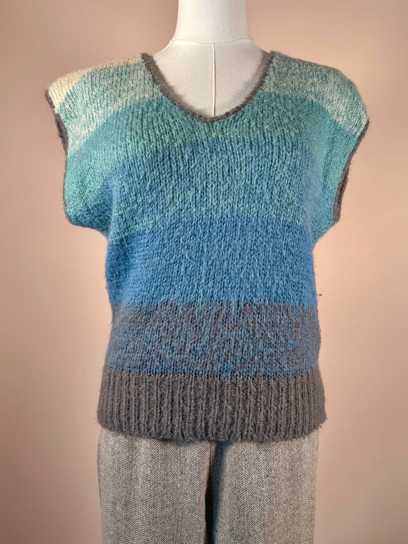 Blue mohair sweater vest with a v-neck and a horizontal striped pattern in varying shades of blue and gray, representing 1970s style.