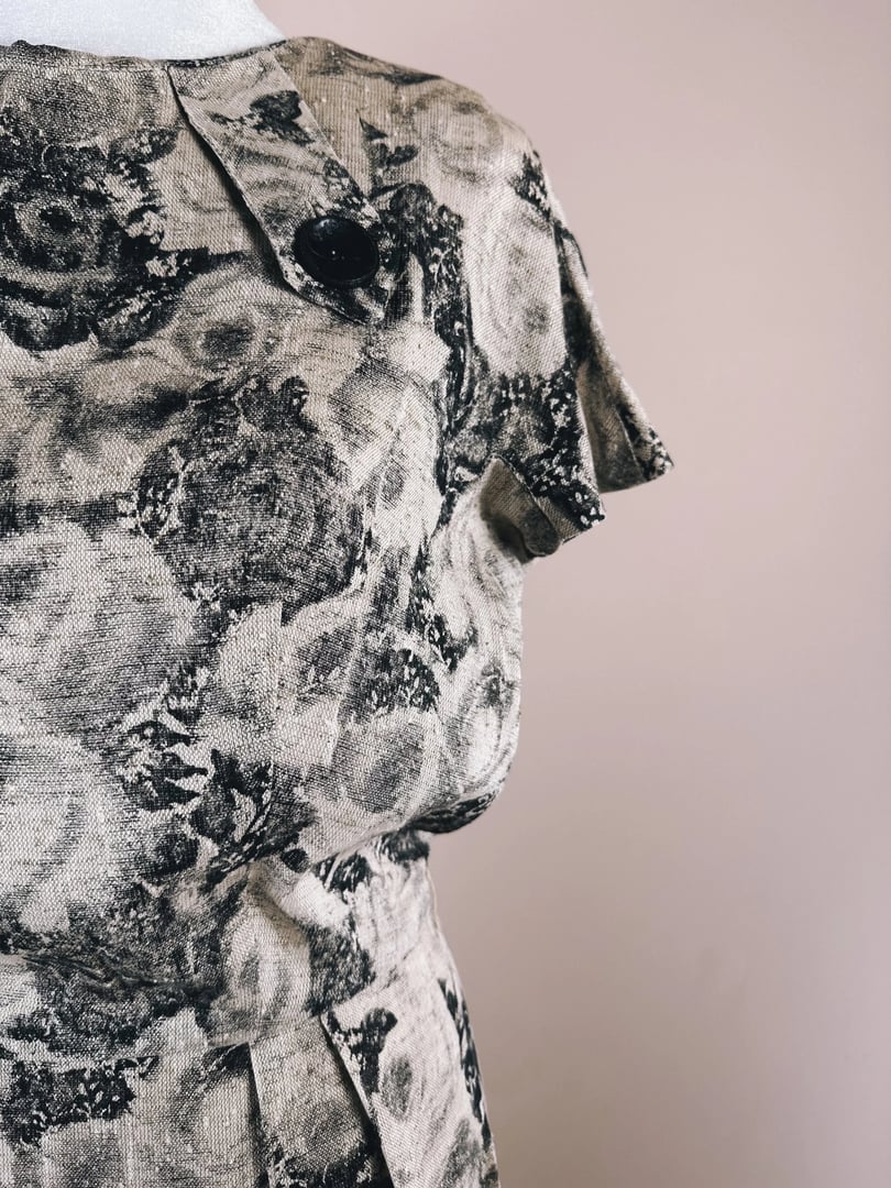Close-up of a vintage-style dress with a floral print and a black button detail on the shoulder.