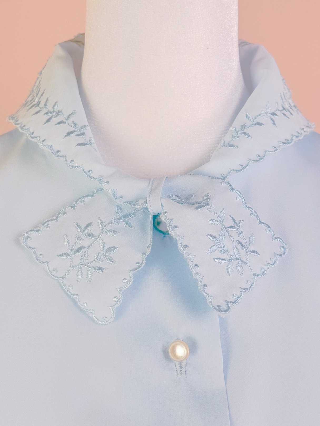 Powder blue blouse featuring an embroidered collar and a pearl button, representing women's 1950s fashion.