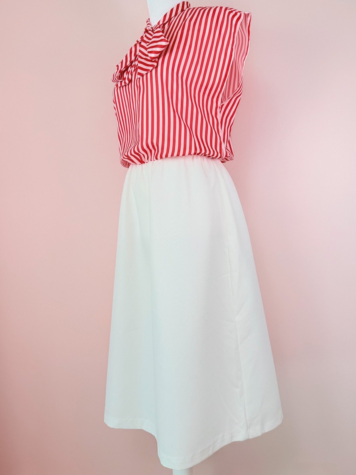 Red and white striped sleeveless top with a bow detail paired with a solid white skirt in a 1970s style women's dress.