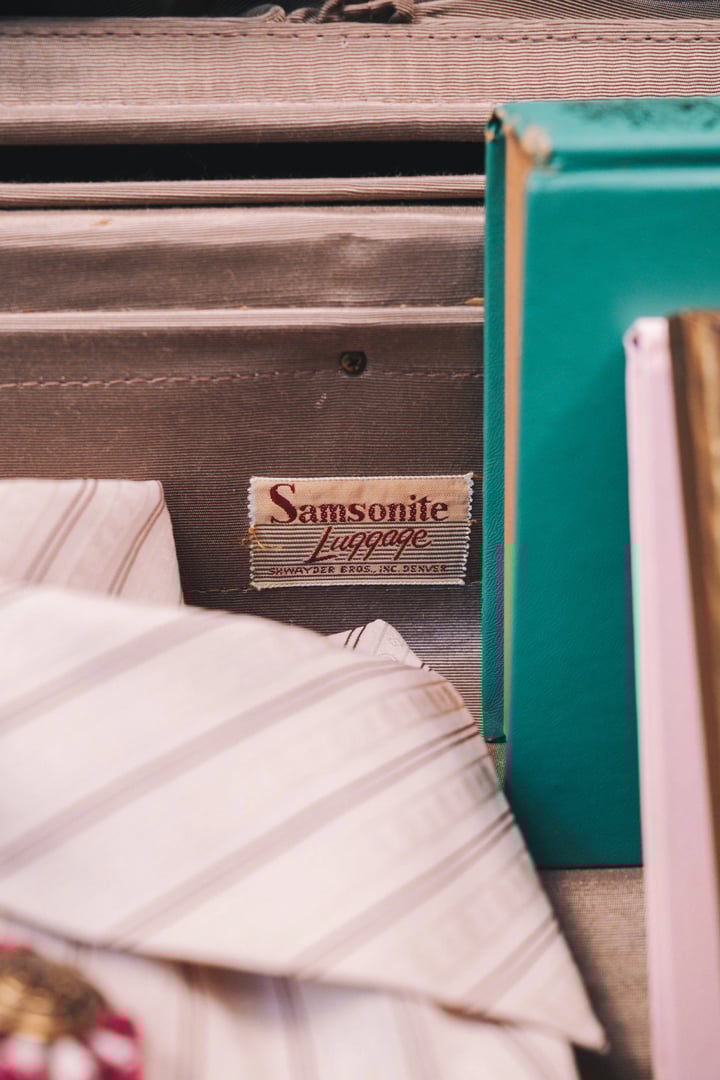 A close-up of a vintage Samsonite luggage tag on a textured surface with various fabrics and boxes.
