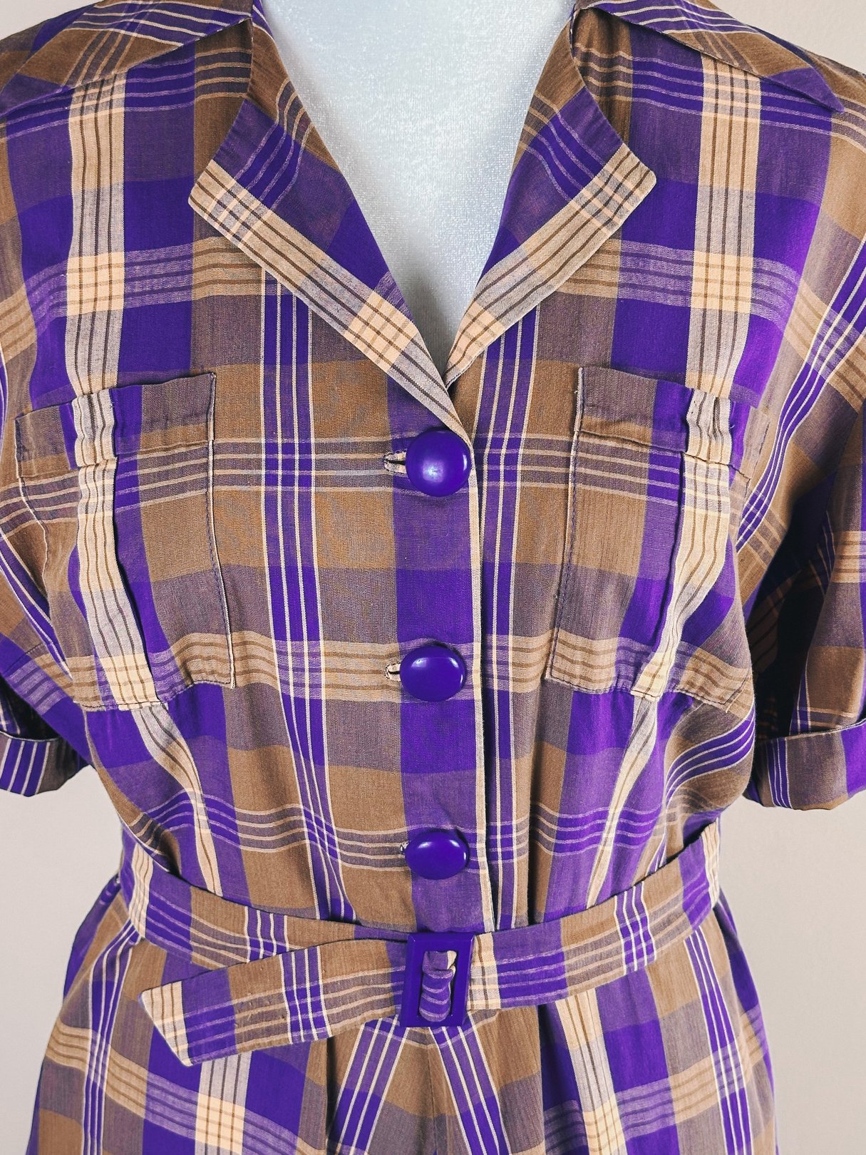 Purple plaid dress featuring short sleeves, a collar, and a belted waist, designed for women in the 1950s.