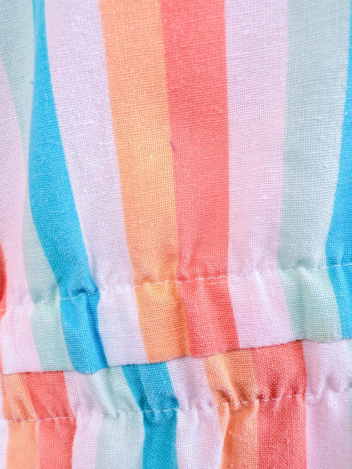 Close-up of a multi-colored striped fabric featuring shades of blue, pink, and orange, showcasing the gathered elastic detail typical of women's 1980s rompers.