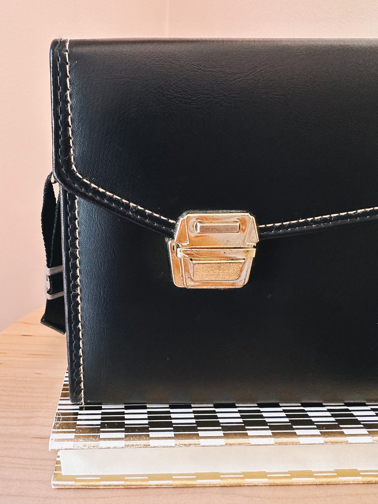 Black leather 1970s-style camera bag with a metal clasp, designed for women.