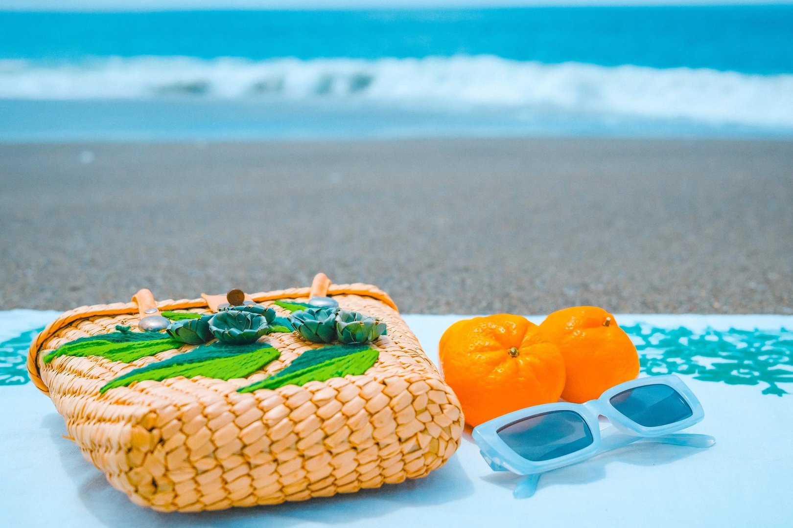 A picnic basket beside two oranges and containers on a beach with waves in the background.